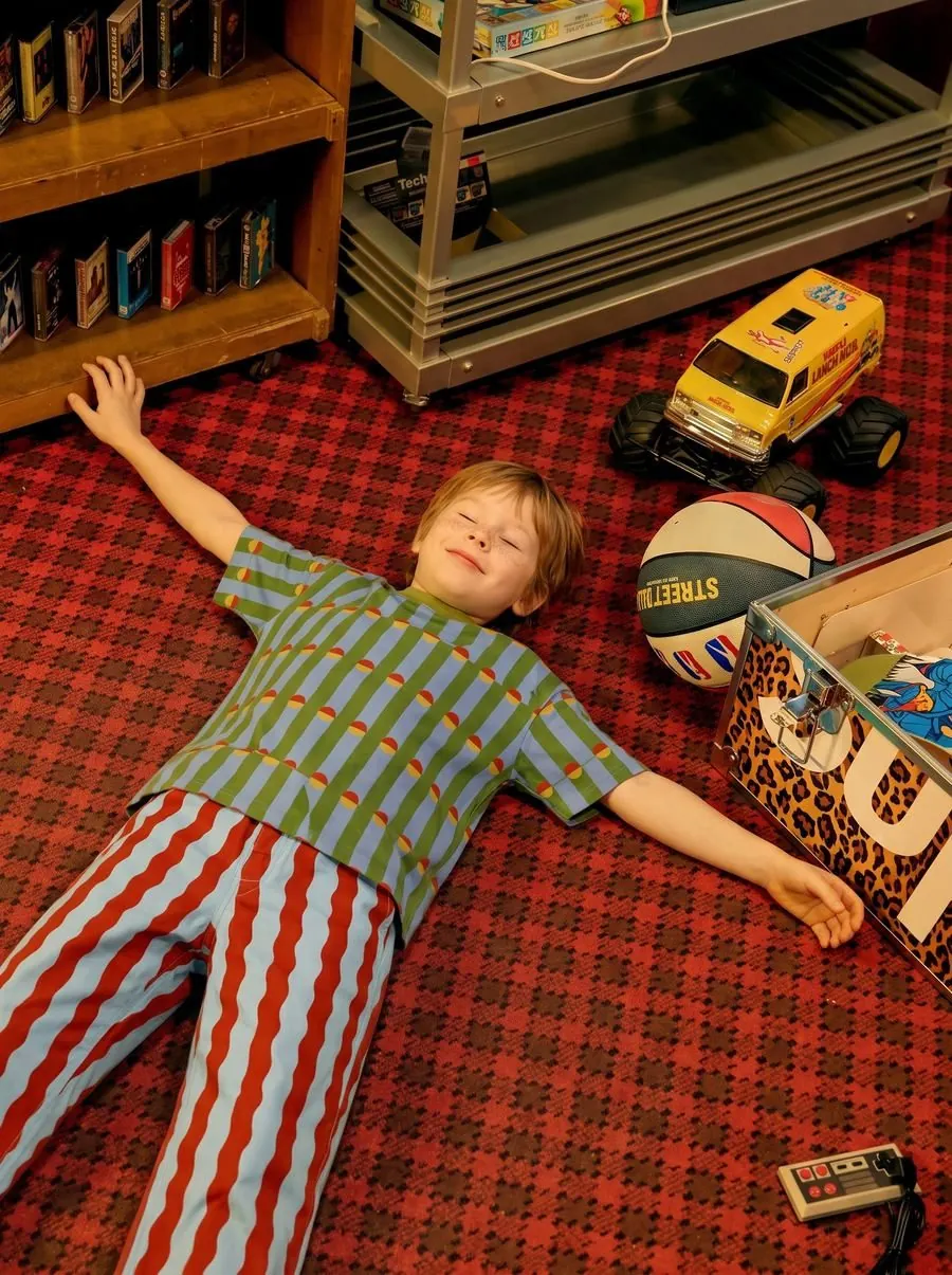Editorial scene of a child lying on a red carpet in the outfit